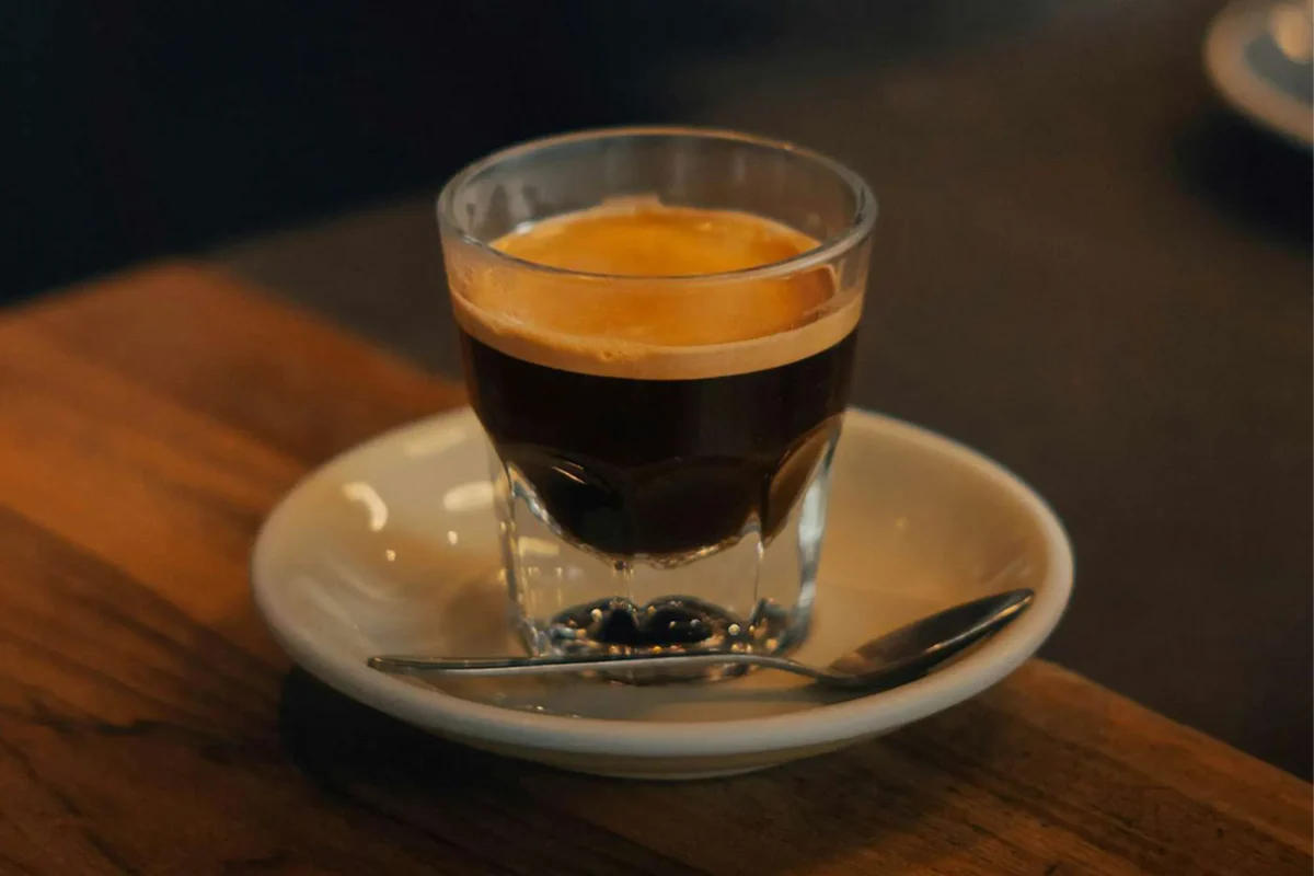 یک شات اسپرسو تازه در لیوان شیشه‌ای روی نعلبکی سفید